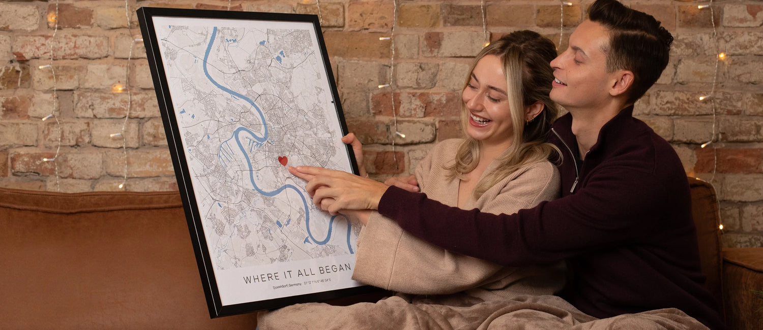Zwei Personen halten ein gerahmtes personalisiertes Stadtplan-Poster mit Herzmarkierung